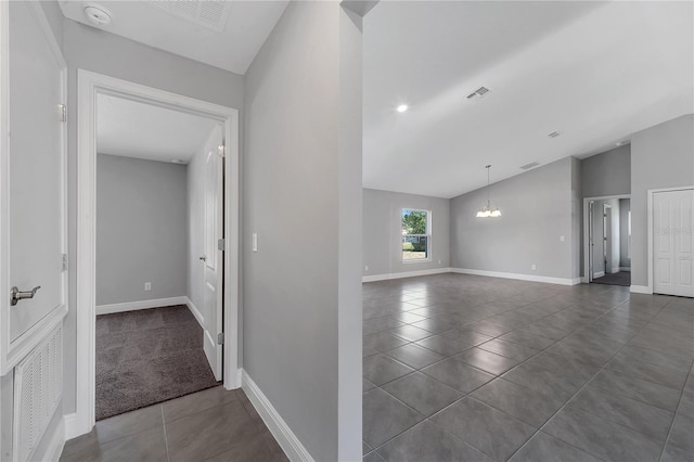 hallway featuring dark tile patterned flooring, lofted ceiling, and an inviting chandelier