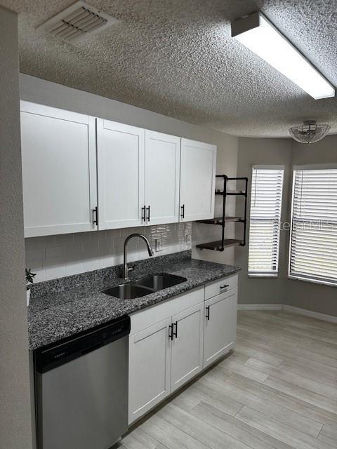 kitchen featuring sink, tasteful backsplash, light hardwood / wood-style flooring, stainless steel dishwasher, and white cabinets