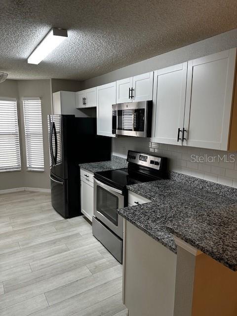 kitchen with stainless steel appliances, white cabinetry, tasteful backsplash, and dark stone counters