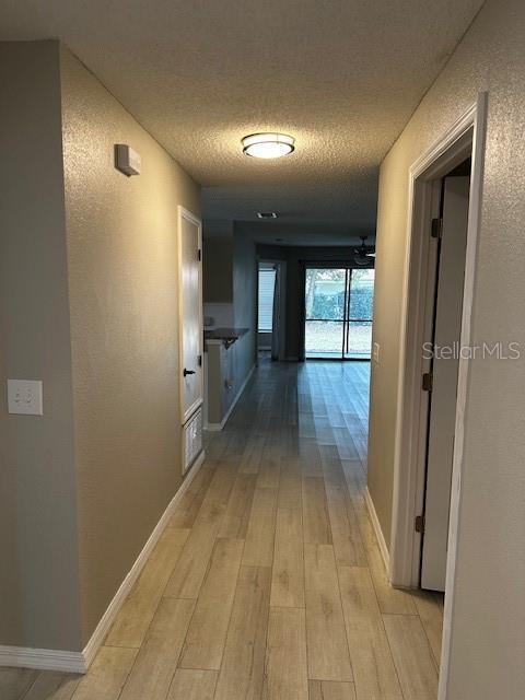 corridor with a textured ceiling and light hardwood / wood-style flooring