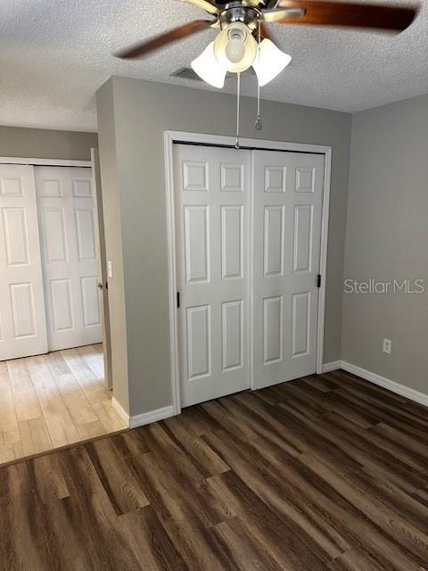 unfurnished bedroom featuring multiple closets, ceiling fan, dark hardwood / wood-style flooring, and a textured ceiling