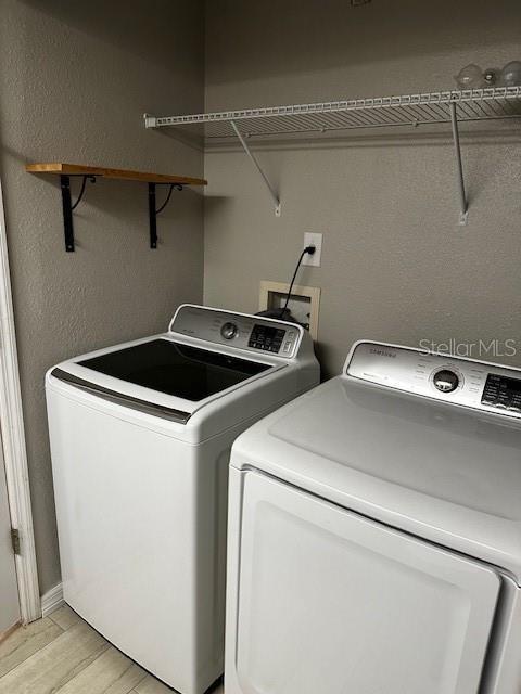 laundry room featuring washing machine and clothes dryer and light hardwood / wood-style flooring