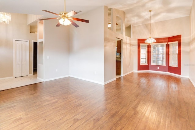 unfurnished living room featuring hardwood / wood-style floors, a towering ceiling, and ceiling fan with notable chandelier