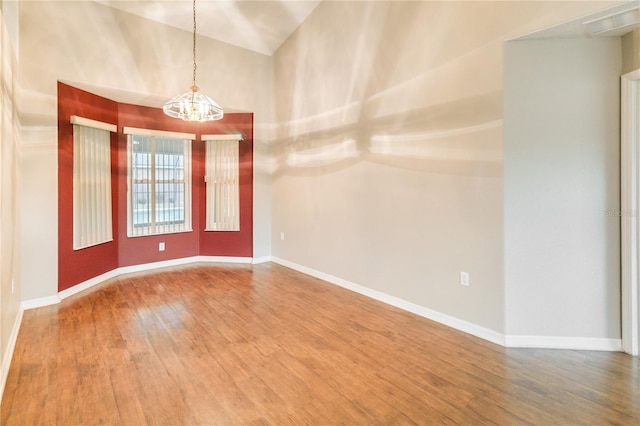 empty room featuring a notable chandelier, hardwood / wood-style flooring, and vaulted ceiling