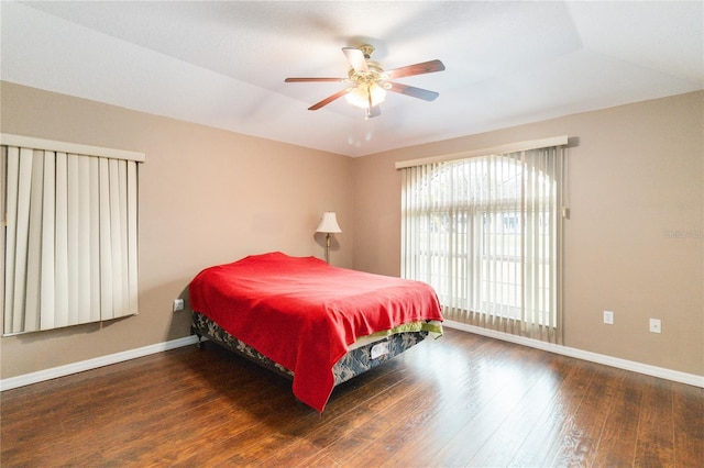 bedroom with a raised ceiling, dark wood-type flooring, and ceiling fan