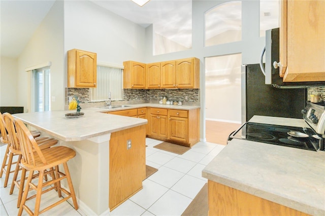 kitchen featuring sink, light tile patterned floors, a breakfast bar area, electric range oven, and kitchen peninsula