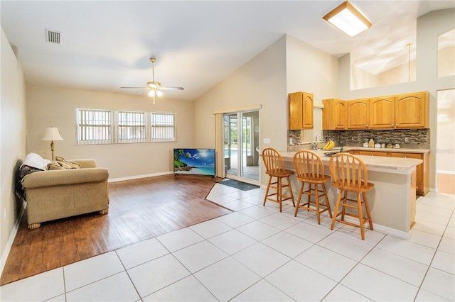 kitchen featuring light tile patterned flooring, backsplash, a kitchen breakfast bar, ceiling fan, and kitchen peninsula