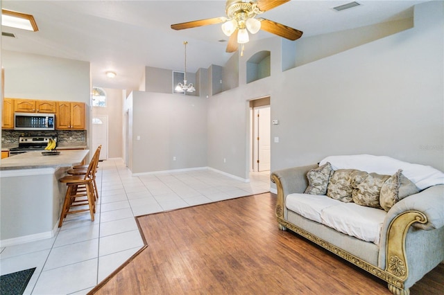 tiled living room featuring high vaulted ceiling and ceiling fan with notable chandelier