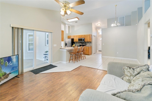 living room with light tile patterned floors, ceiling fan with notable chandelier, and vaulted ceiling