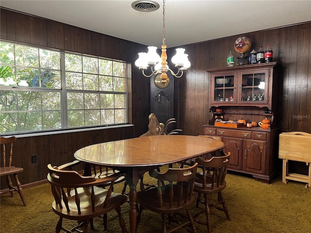 dining area with dark colored carpet, a notable chandelier, and wood walls