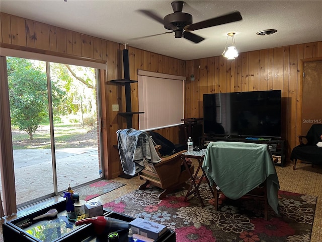 living room with carpet, ceiling fan, wood walls, and a textured ceiling