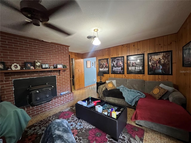 living room with a wood stove, wooden walls, ceiling fan, a textured ceiling, and carpet floors