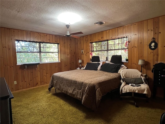 carpeted bedroom featuring multiple windows, ceiling fan, and wooden walls