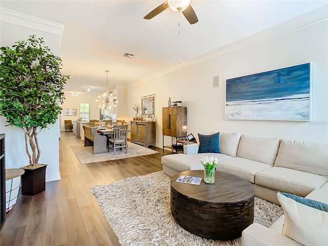 living room featuring hardwood / wood-style floors, ceiling fan with notable chandelier, and crown molding