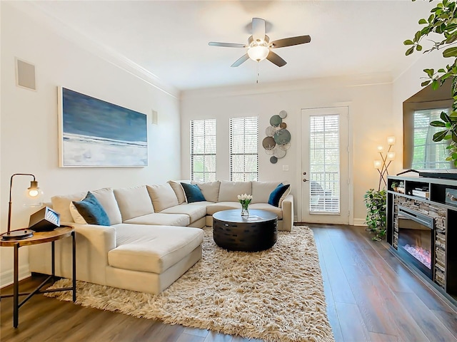 living room featuring wood-type flooring, a stone fireplace, ceiling fan, and ornamental molding