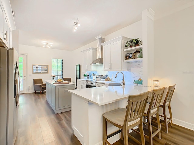 kitchen featuring kitchen peninsula, appliances with stainless steel finishes, sink, wall chimney range hood, and white cabinets