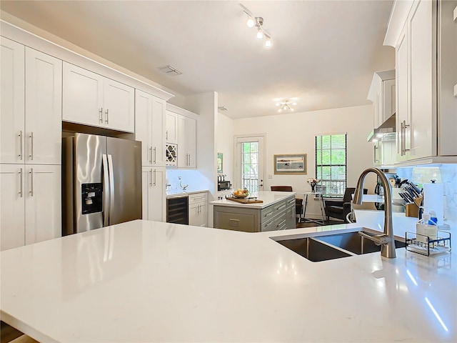 kitchen with kitchen peninsula, stainless steel refrigerator with ice dispenser, beverage cooler, sink, and white cabinets