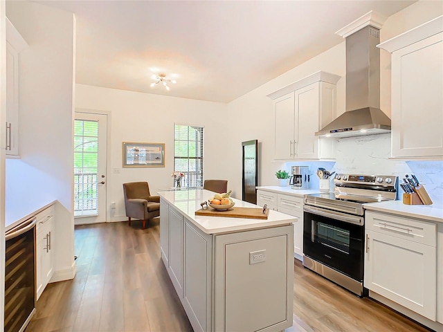 kitchen with white cabinetry, wall chimney range hood, a kitchen island, stainless steel range with electric cooktop, and light wood-type flooring