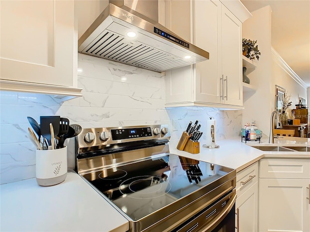 kitchen with white cabinets, electric stove, sink, wall chimney range hood, and decorative backsplash