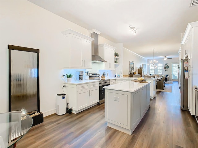 kitchen featuring kitchen peninsula, stainless steel appliances, wall chimney range hood, white cabinets, and hanging light fixtures