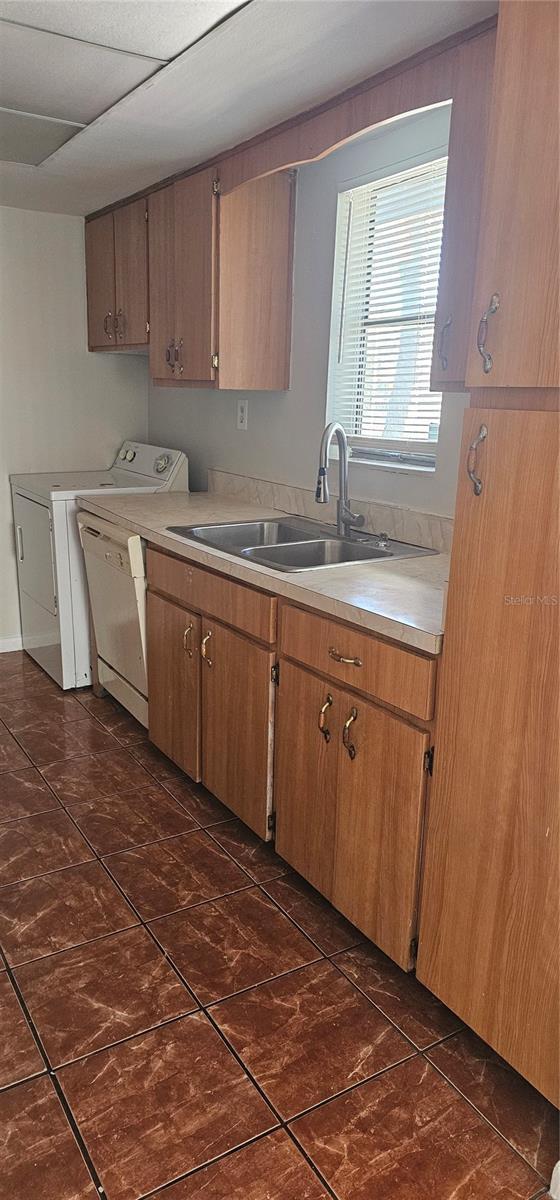 kitchen featuring dishwasher, washer / dryer, a drop ceiling, and sink