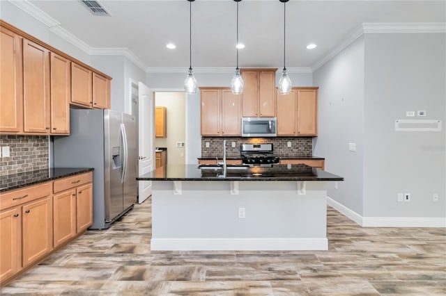 kitchen featuring light wood-type flooring, stainless steel appliances, a kitchen island with sink, and dark stone counters