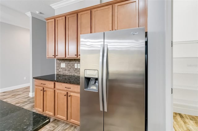 kitchen featuring tasteful backsplash, stainless steel refrigerator with ice dispenser, crown molding, dark stone counters, and light hardwood / wood-style floors