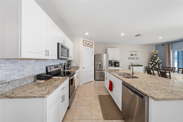 kitchen with a center island with sink, sink, light stone counters, white cabinetry, and stainless steel appliances