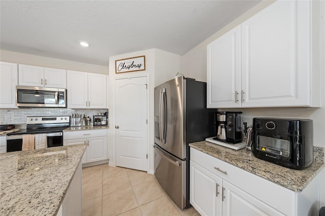 kitchen with white cabinets, appliances with stainless steel finishes, light tile patterned floors, and light stone counters