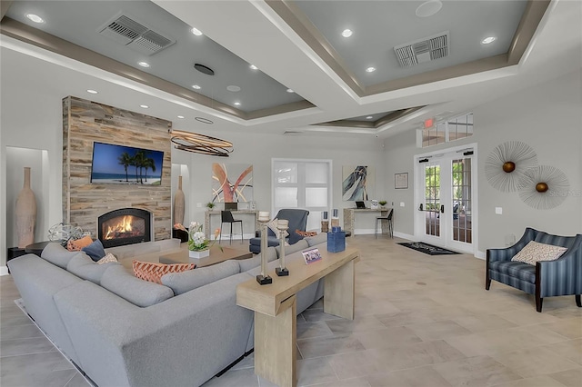 living room featuring french doors, a raised ceiling, and a tiled fireplace