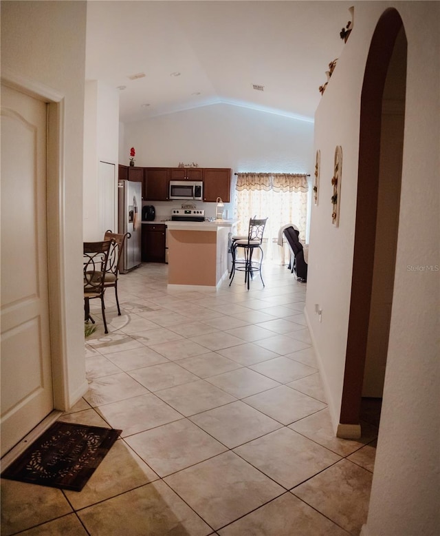 kitchen featuring a center island, lofted ceiling, light tile patterned floors, appliances with stainless steel finishes, and a kitchen bar