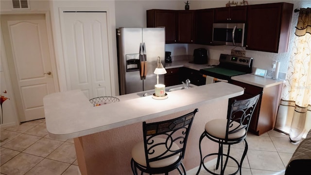 kitchen with a kitchen bar, a center island with sink, light tile patterned flooring, and appliances with stainless steel finishes