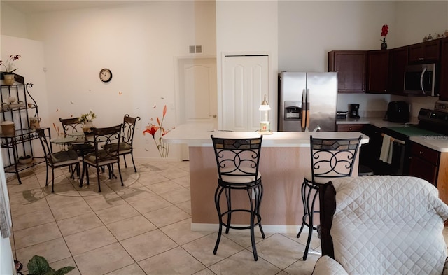 kitchen featuring a kitchen bar, light tile patterned floors, dark brown cabinetry, and appliances with stainless steel finishes