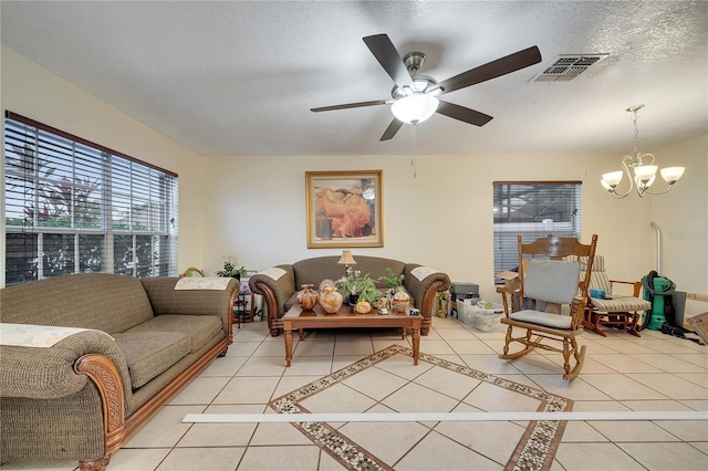 living room featuring tile patterned flooring, ceiling fan with notable chandelier, and a textured ceiling