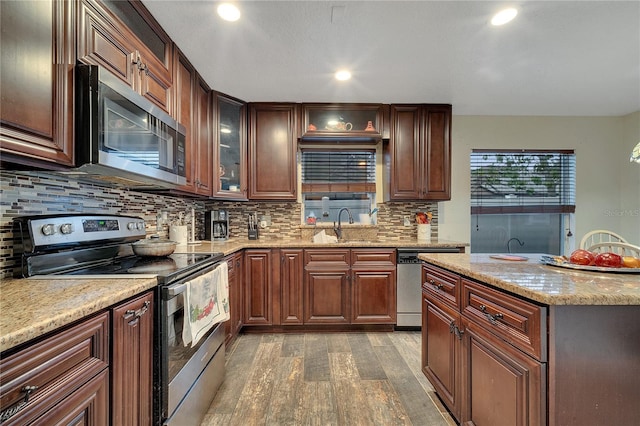 kitchen with sink, light stone counters, light wood-type flooring, appliances with stainless steel finishes, and decorative backsplash