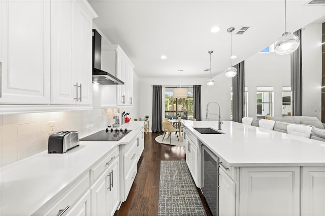 kitchen with dark wood-type flooring, a center island with sink, sink, wall chimney exhaust hood, and black electric cooktop