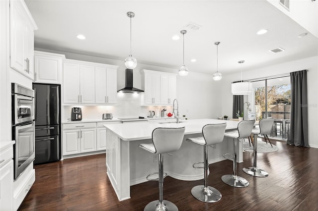 kitchen with white cabinetry, dark hardwood / wood-style flooring, an island with sink, and wall chimney range hood