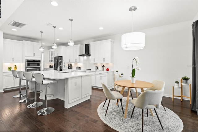 kitchen featuring a center island with sink, white cabinetry, and wall chimney exhaust hood