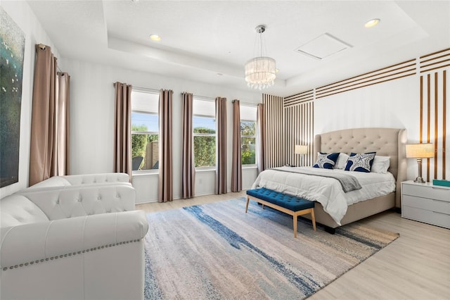 bedroom with a notable chandelier, light hardwood / wood-style flooring, and a tray ceiling