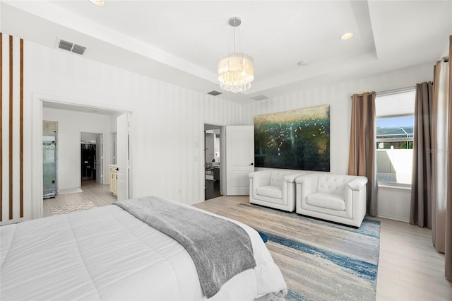 bedroom with a notable chandelier, light wood-type flooring, and a tray ceiling