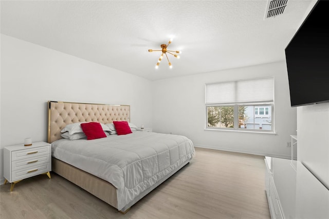 bedroom with light wood-type flooring, a textured ceiling, and a chandelier