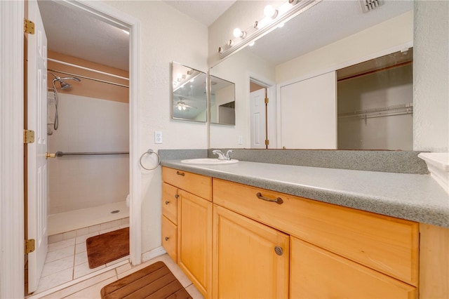 bathroom featuring tile patterned flooring, a tile shower, vanity, and a textured ceiling