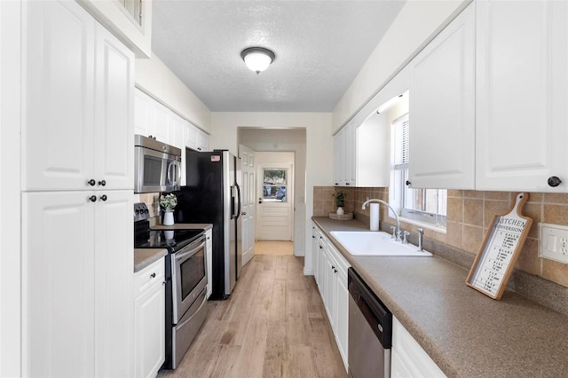 kitchen with white cabinetry, sink, stainless steel appliances, light hardwood / wood-style flooring, and backsplash