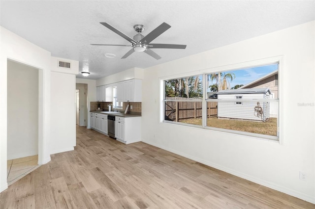 unfurnished living room featuring a wealth of natural light, sink, a textured ceiling, and light wood-type flooring