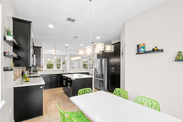 kitchen with appliances with stainless steel finishes, tasteful backsplash, sink, decorative light fixtures, and a center island