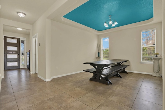 tiled dining area featuring baseboards, a raised ceiling, and a notable chandelier