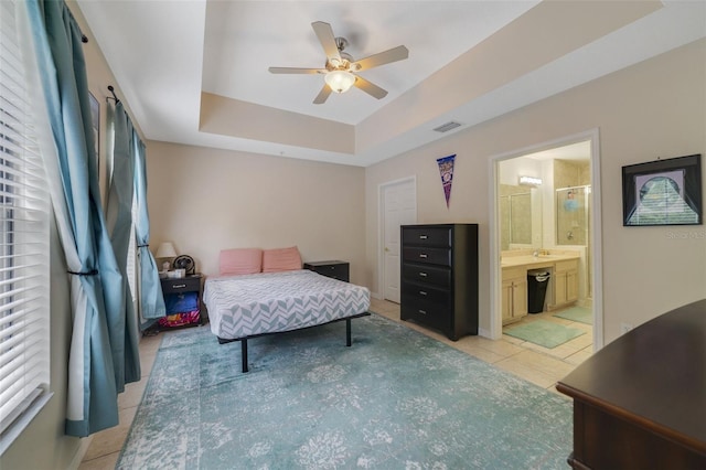 bedroom with a tray ceiling, ensuite bath, ceiling fan, and light tile patterned flooring