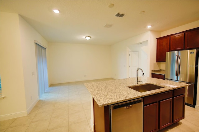 kitchen with sink, light tile patterned floors, appliances with stainless steel finishes, a kitchen island with sink, and light stone counters