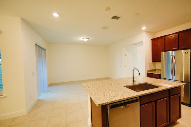 kitchen featuring a kitchen island with sink, sink, light stone counters, and appliances with stainless steel finishes