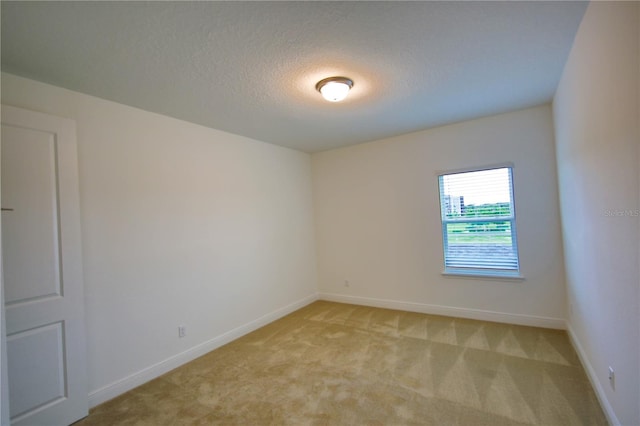 empty room with light colored carpet and a textured ceiling